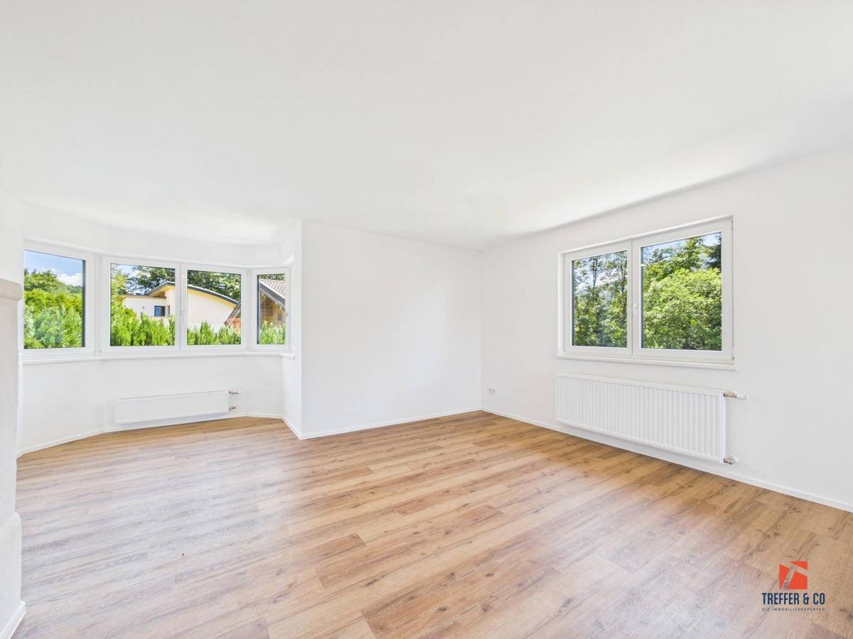 Lichtdurchflutetes Wohnzimmer mit Holzboden und großen Fenstern, die eine weite Aussicht bieten.