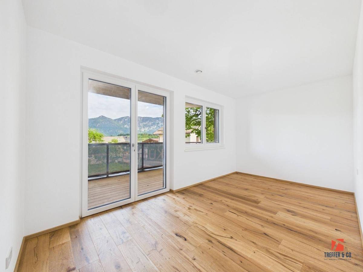 Helles Schlafzimmer mit Holzboden, großen Fenstern und Zugang zum Balkon.