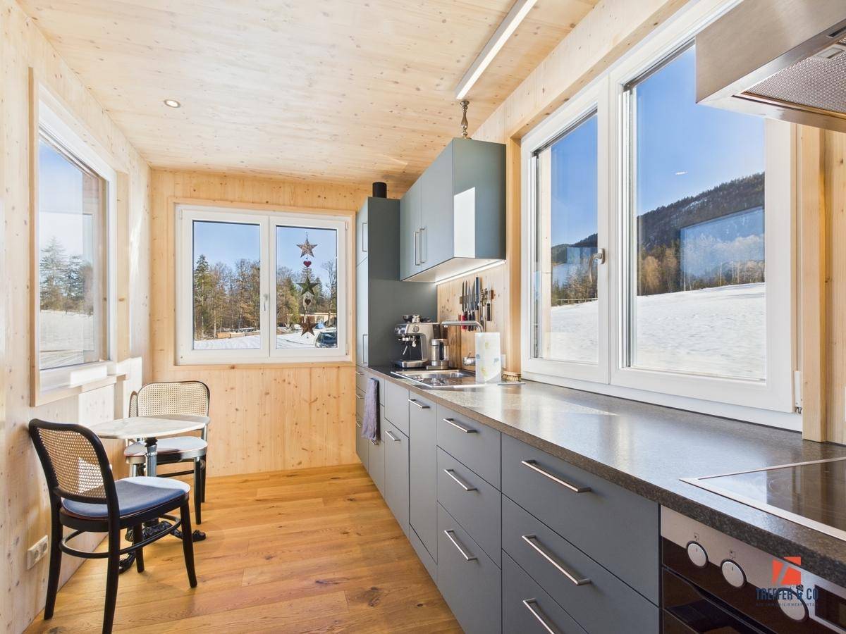 Moderne Einbauküche mit Holzdetails, blaugrauen Fronten und weitem Blick in die Natur.