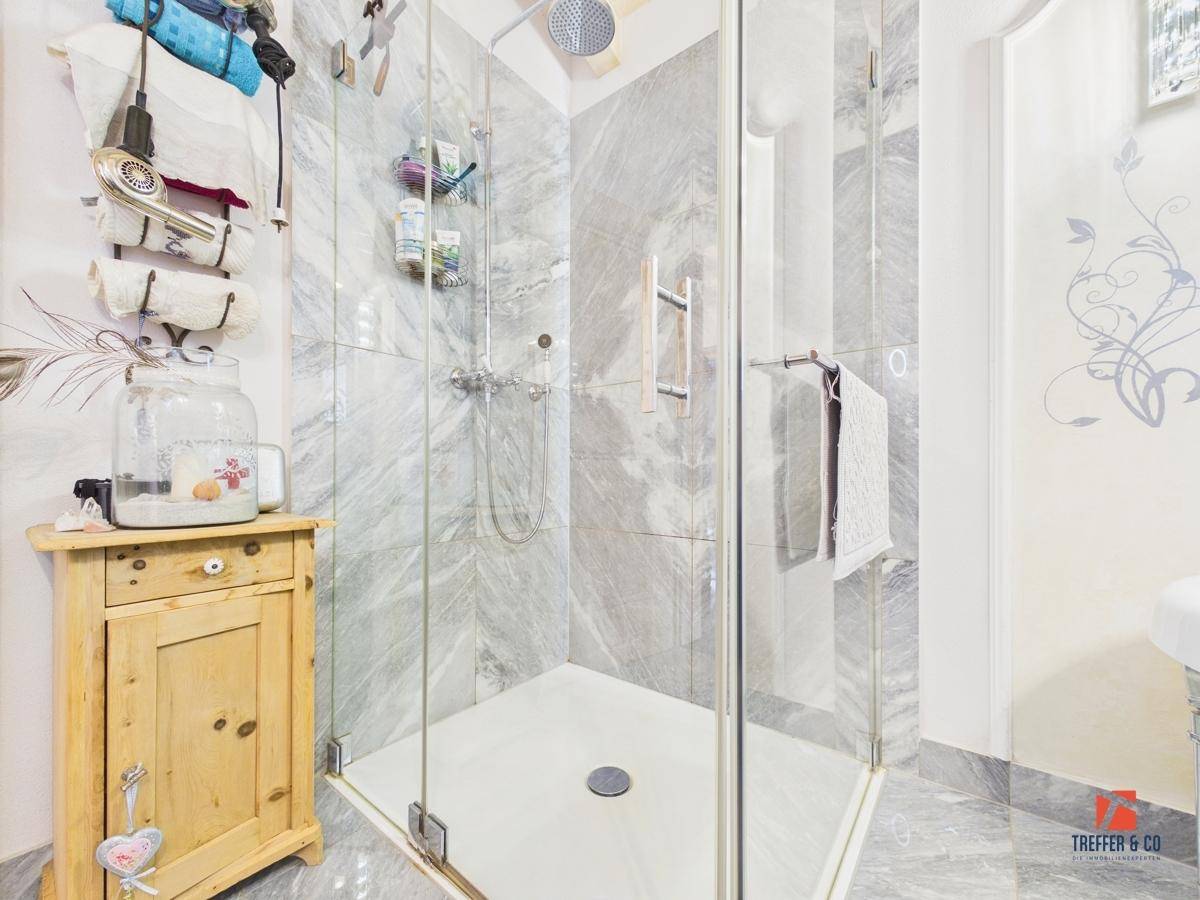 Begehbare Dusche mit Glasabtrennung und modernen Fliesen in einem hellen Badezimmer.
