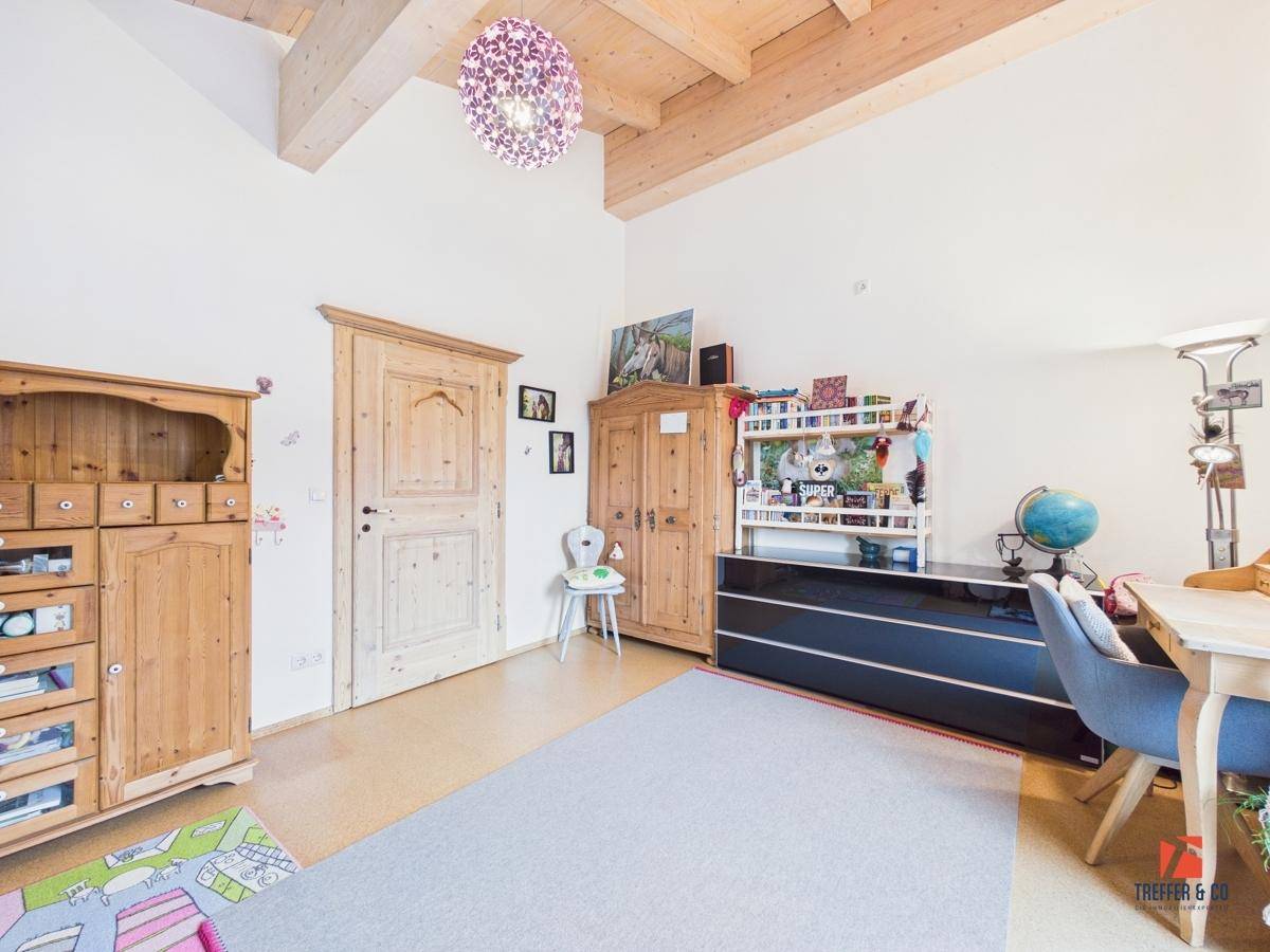 Kinderzimmer mit Holzbalkendecke, Holzmöbeln und einem Schreibtisch, der zum Lernen einlädt.