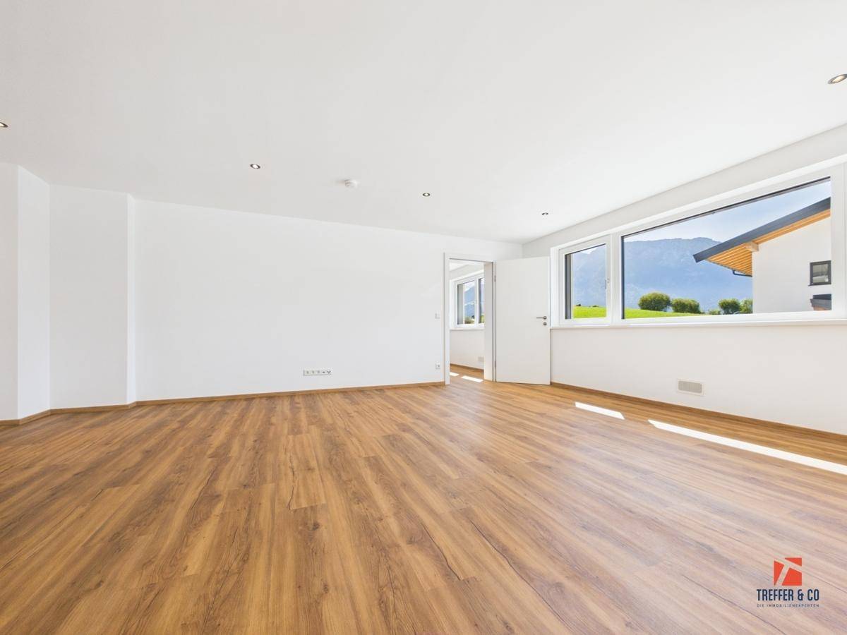 Geräumiges Wohnzimmer mit Laminatboden, weißen Wänden und weitem Blick auf die Berge.