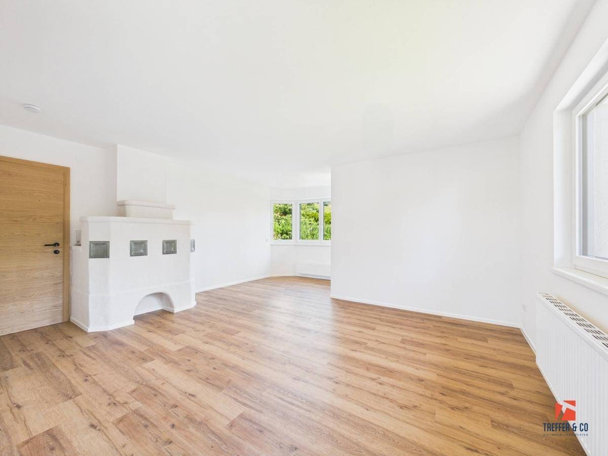 Geräumiges Wohnzimmer mit Holzboden und traditionellem Kachelofen als Blickfang.