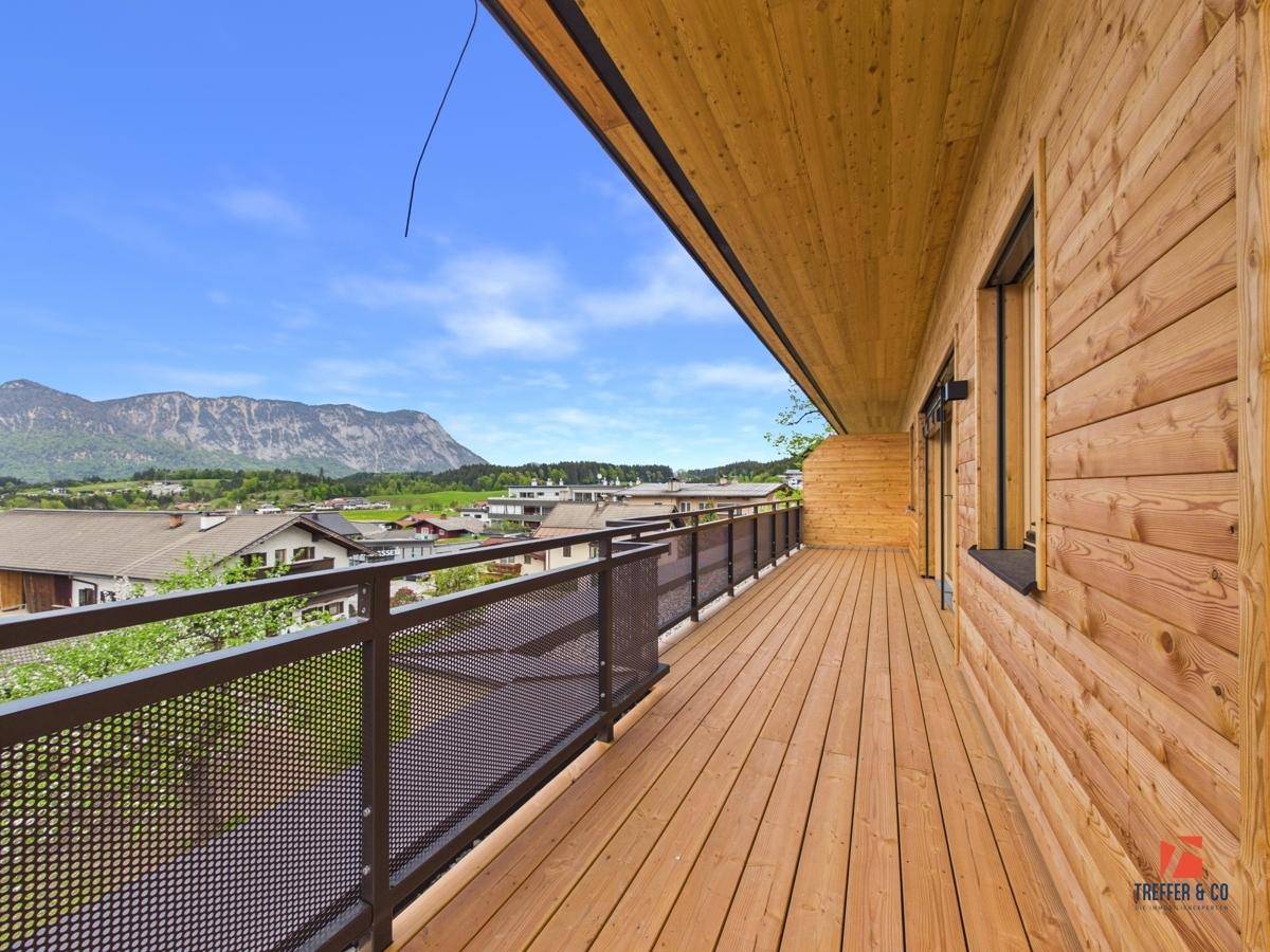 Langer Holzbalkon mit Metallgeländer und weitem Blick auf die grüne Landschaft und Berge.