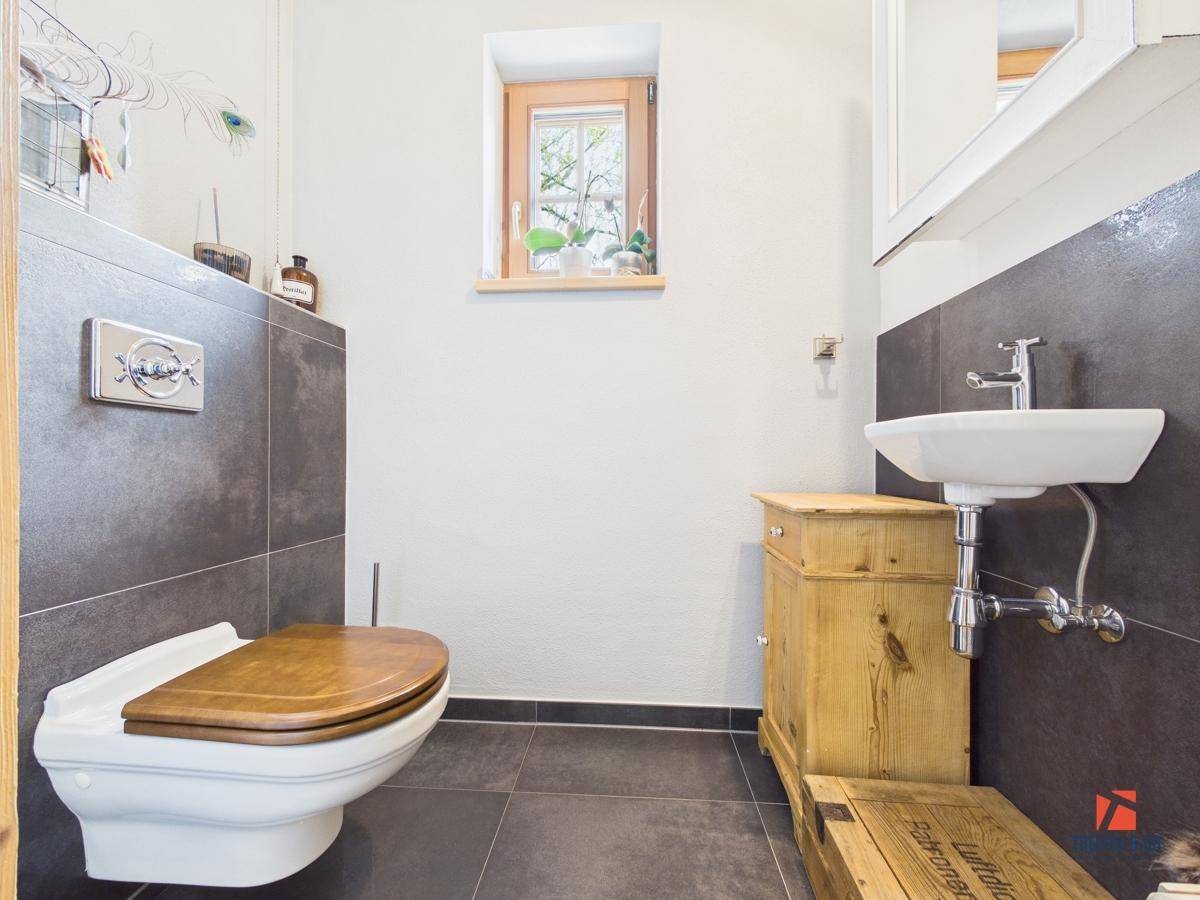 Gäste-WC mit dunklen Fliesen, Holzwaschtisch und einem kleinen Fenster für natürliche Belüftung.