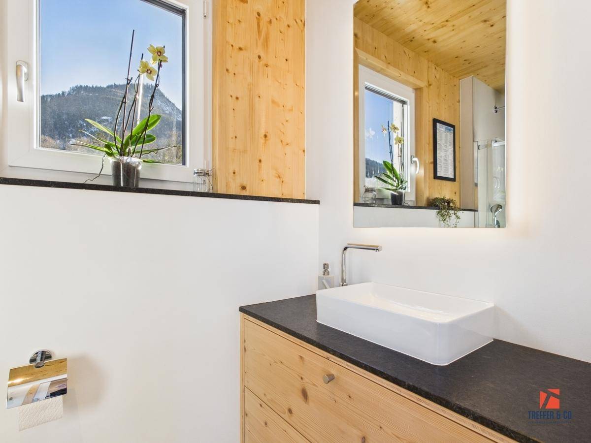Badezimmer mit modernem Aufsatzwaschbecken, beleuchtetem Spiegel und Fenster mit Bergblick.