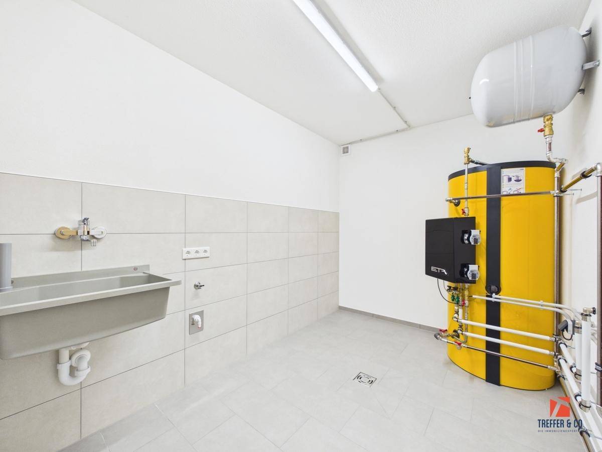 Technikraum mit großem Warmwasserspeicher und Waschbecken, ideal für den Hauswirtschaftsbereich.