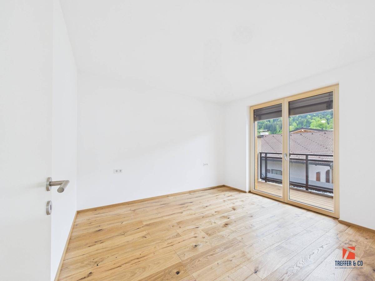 Helles Schlafzimmer mit Holzboden und Zugang zu einem Balkon mit Blick auf die Umgebung.
