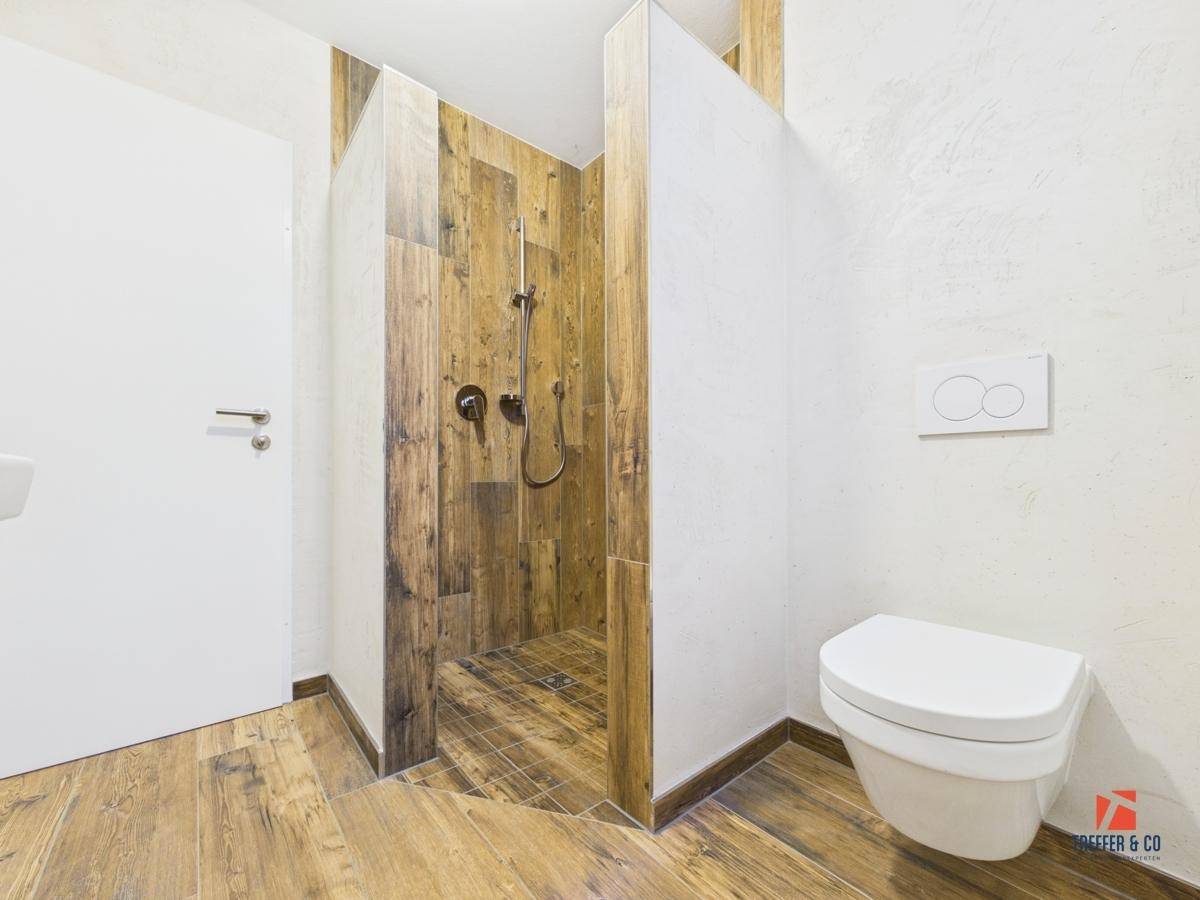 Modernes Badezimmer mit Holzoptik-Fliesen, wandhängendem WC und begehbarer Dusche.