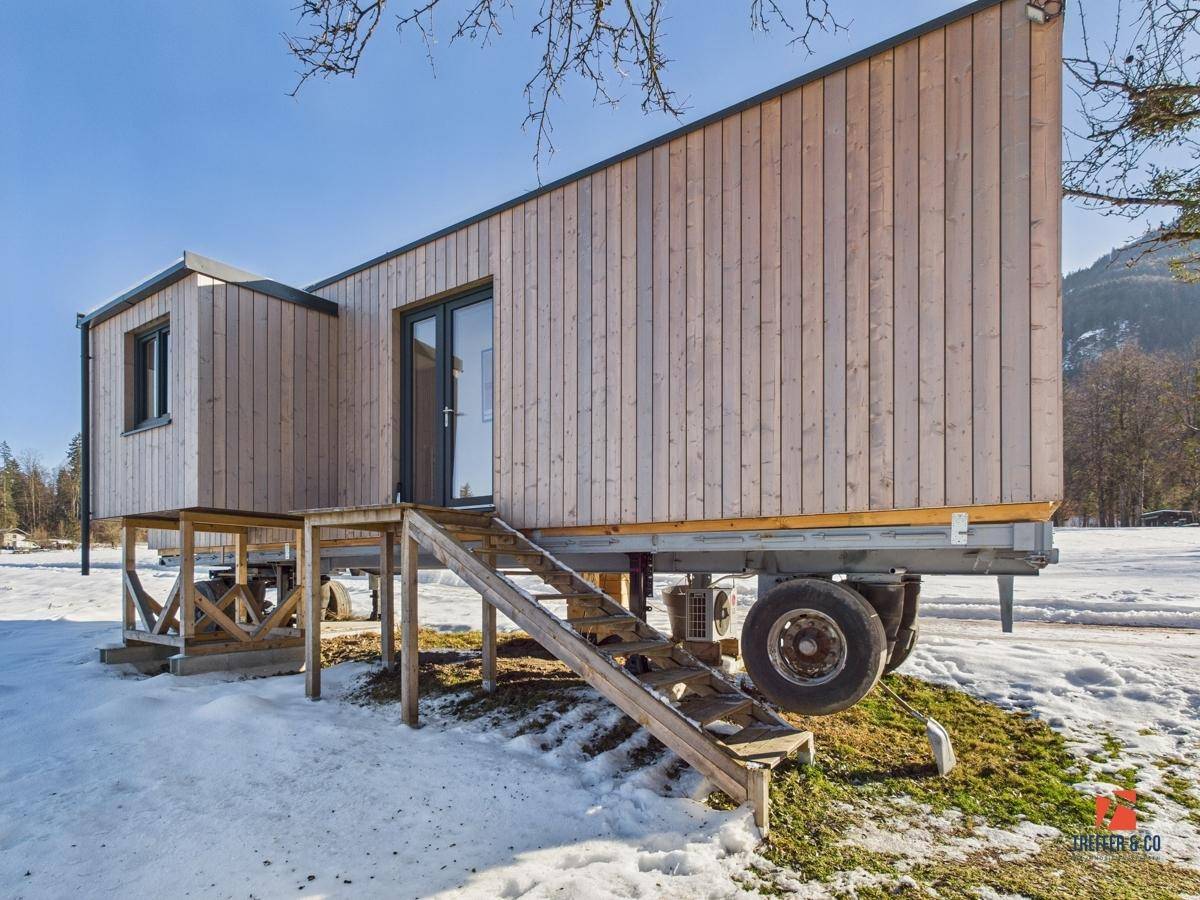 Seitenansicht des Tiny Houses auf Rädern, eingebettet in eine winterliche Naturlandschaft mit Bäumen.