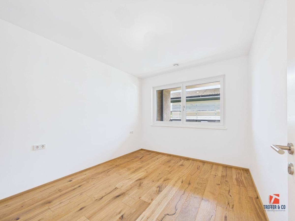 Unmöbliertes Schlafzimmer mit Holzboden und einem großen Fenster für viel Tageslicht.