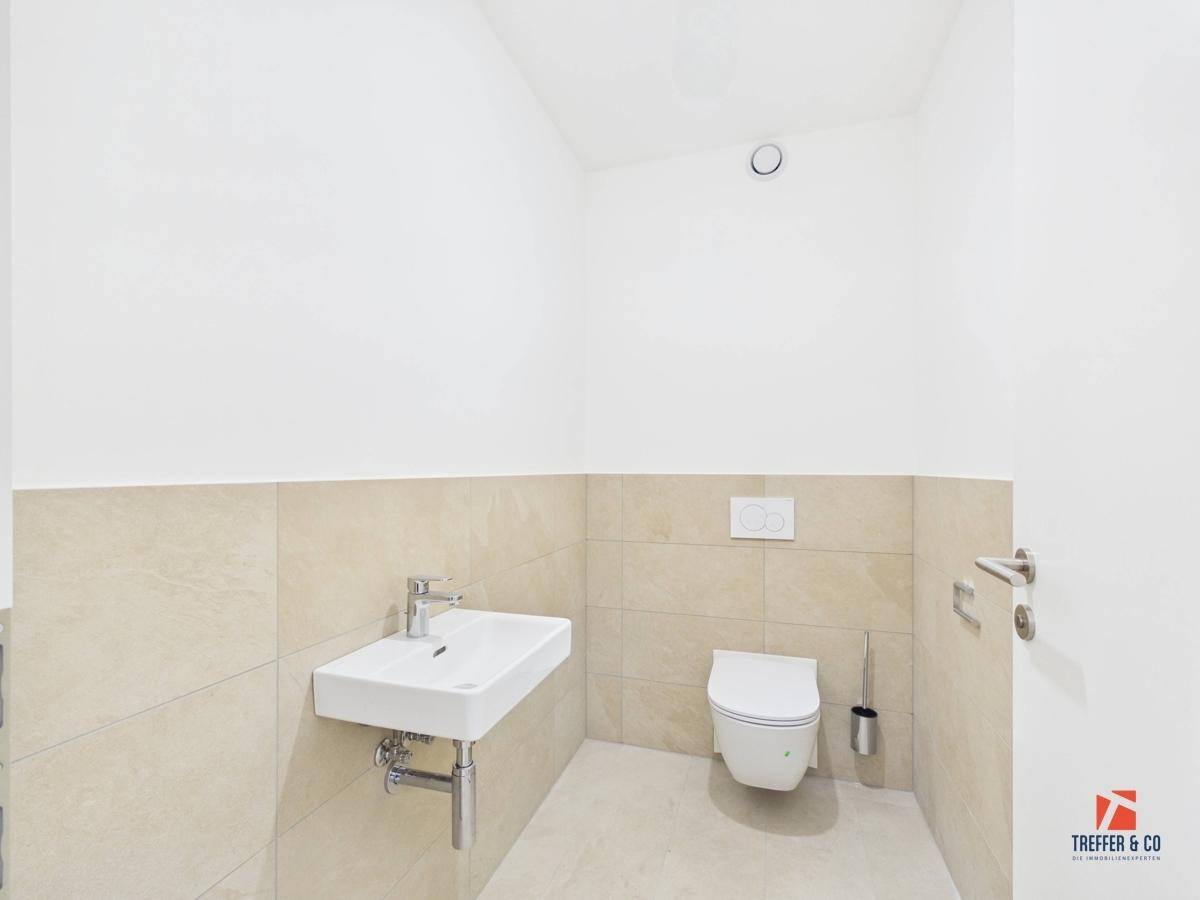 Kleines Gäste-WC mit wandhängendem WC, Waschbecken und beigefarbenen Fliesen.