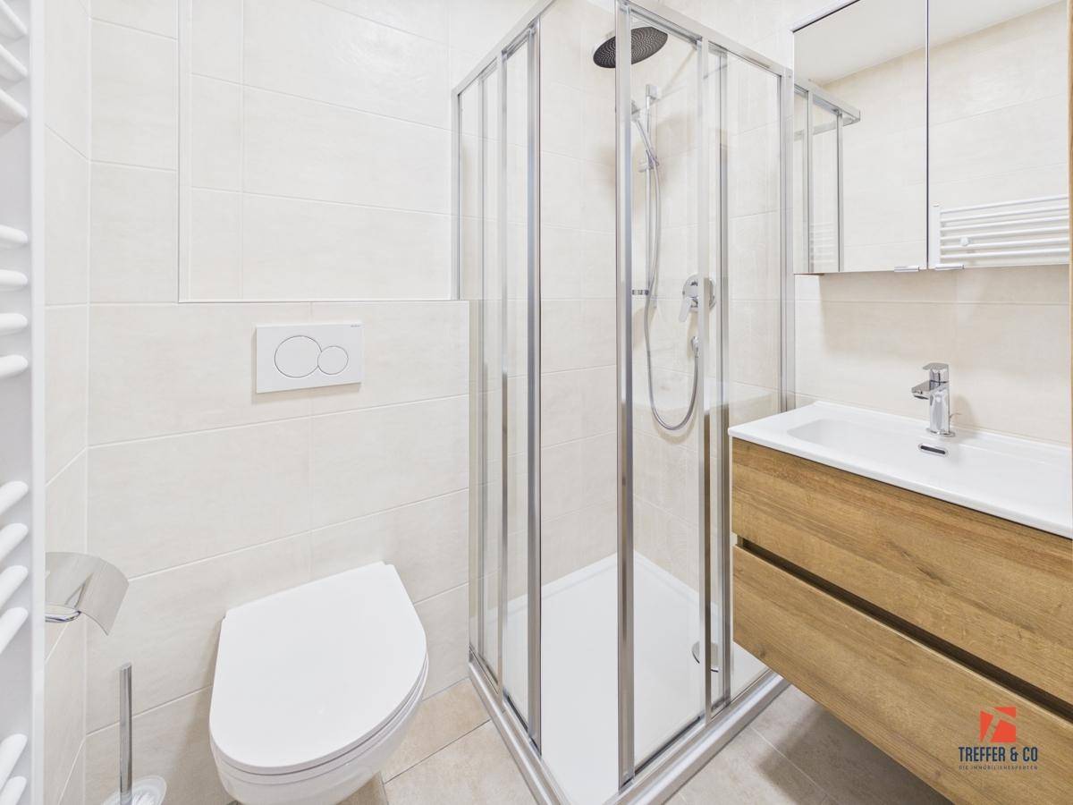 Modernes Badezimmer mit Dusche, Toilette und Waschbecken mit Holzunterschrank.