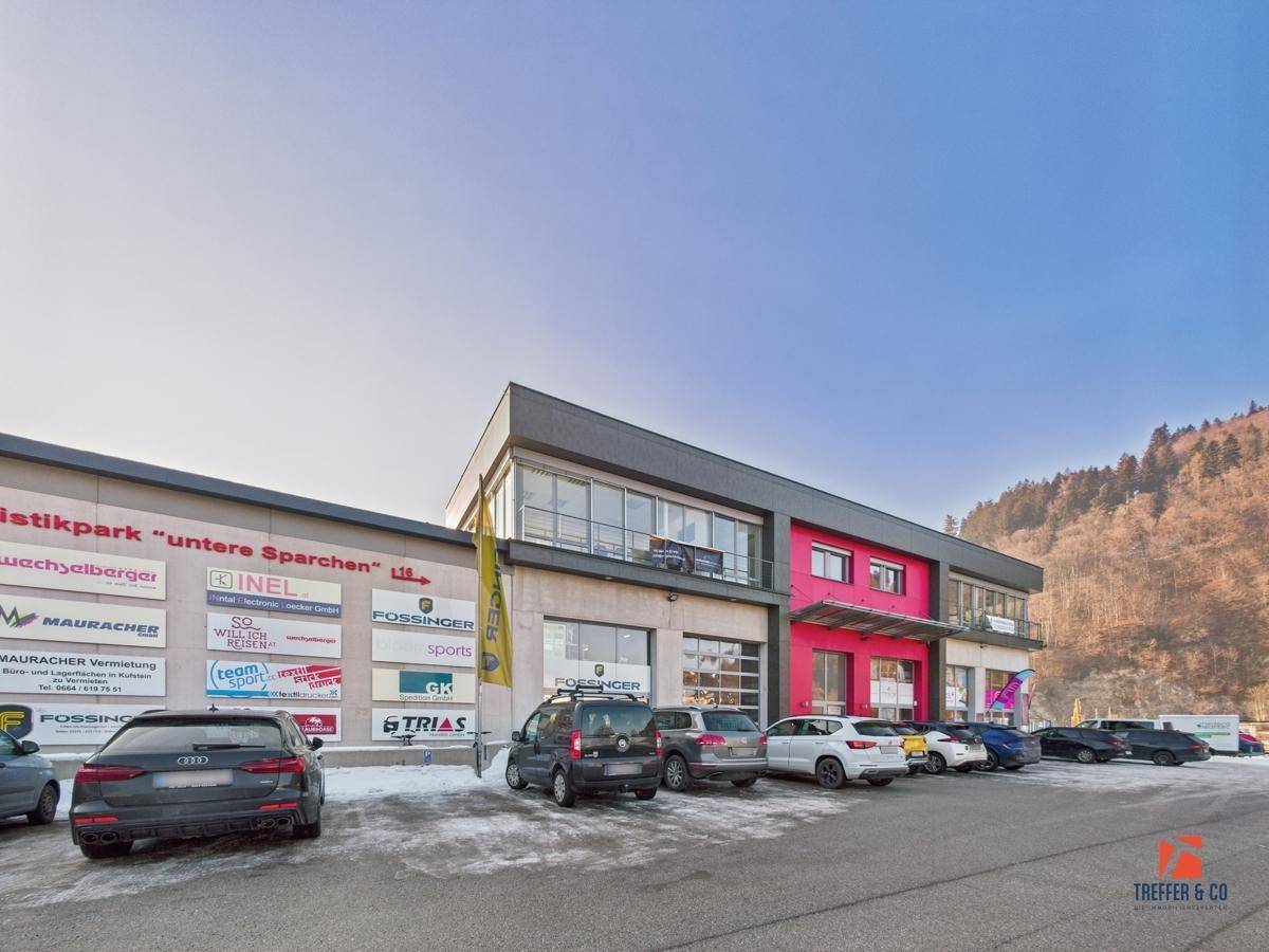 Modernes Geschäftsgebäude mit großem Parkplatz und verschiedenen Firmenlogos an der Fassade.