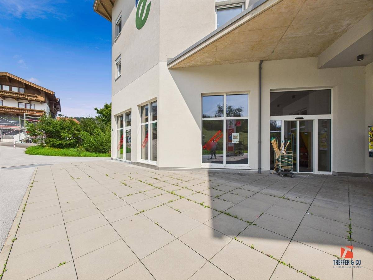 Gepflasterter Vorplatz vor dem Geschäftsgebäude mit großen Fenstern und Blick auf die Umgebung.