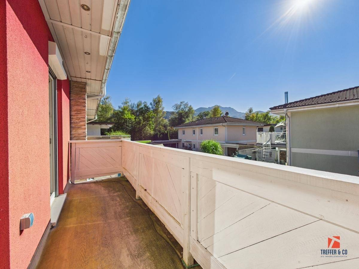 Sonniger Balkon mit weißem Holzgeländer und Blick auf die umliegende Landschaft.