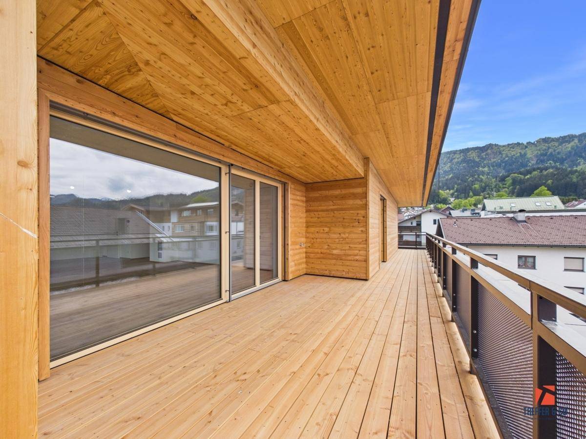 Langer Holzbalkon mit Metallgeländer und weitem Blick auf die Umgebung und Berge.