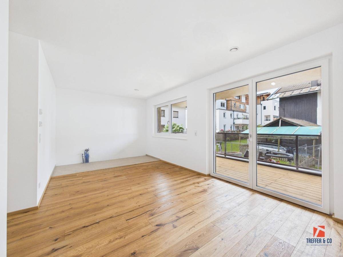Heller Wohnbereich mit Holzboden und großen Schiebetüren, die auf einen Balkon führen.