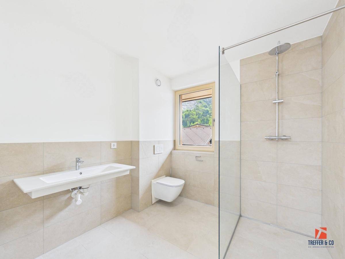 Modernes Badezimmer mit Fenster, großer Dusche, wandhängendem WC und beigefarbenen Fliesen.