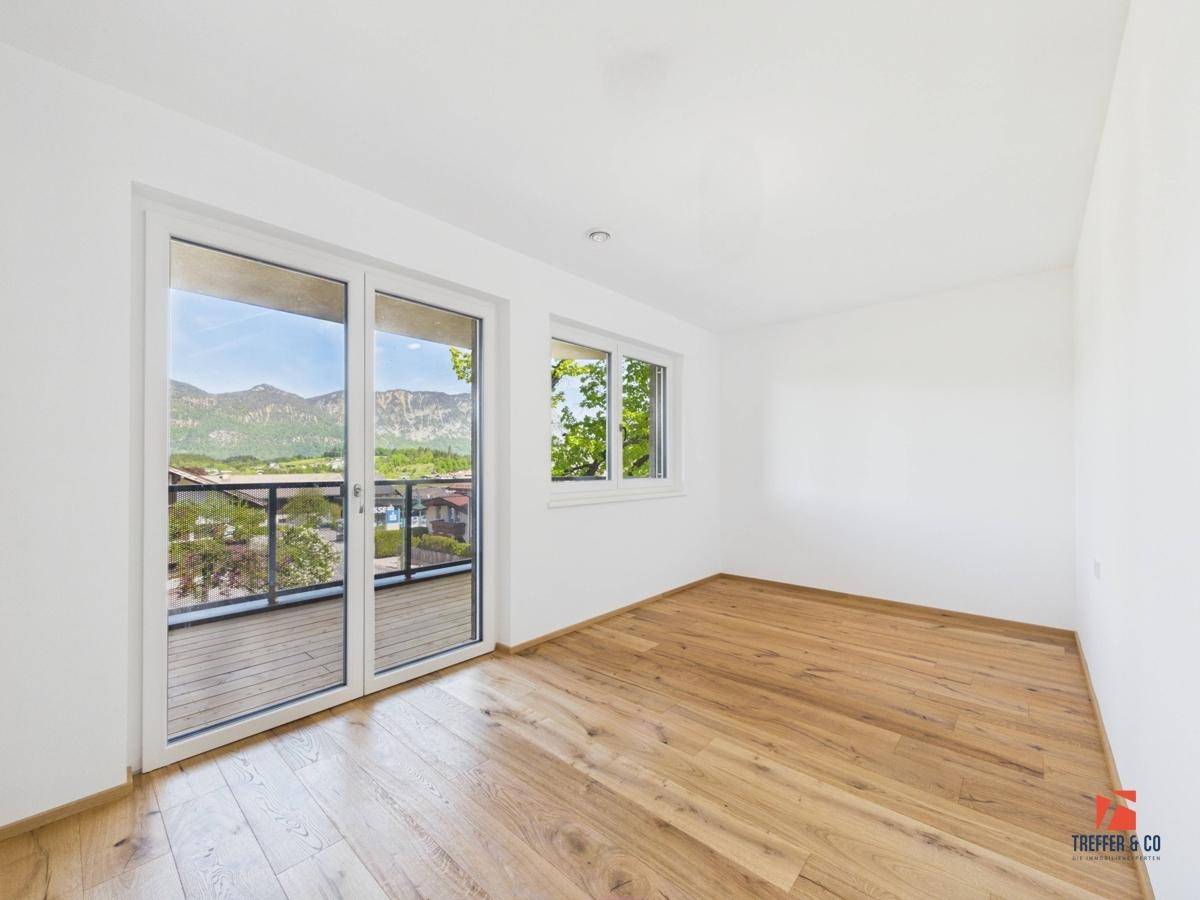Helles Schlafzimmer mit Holzboden, großem Balkonzugang und weitem Bergblick.