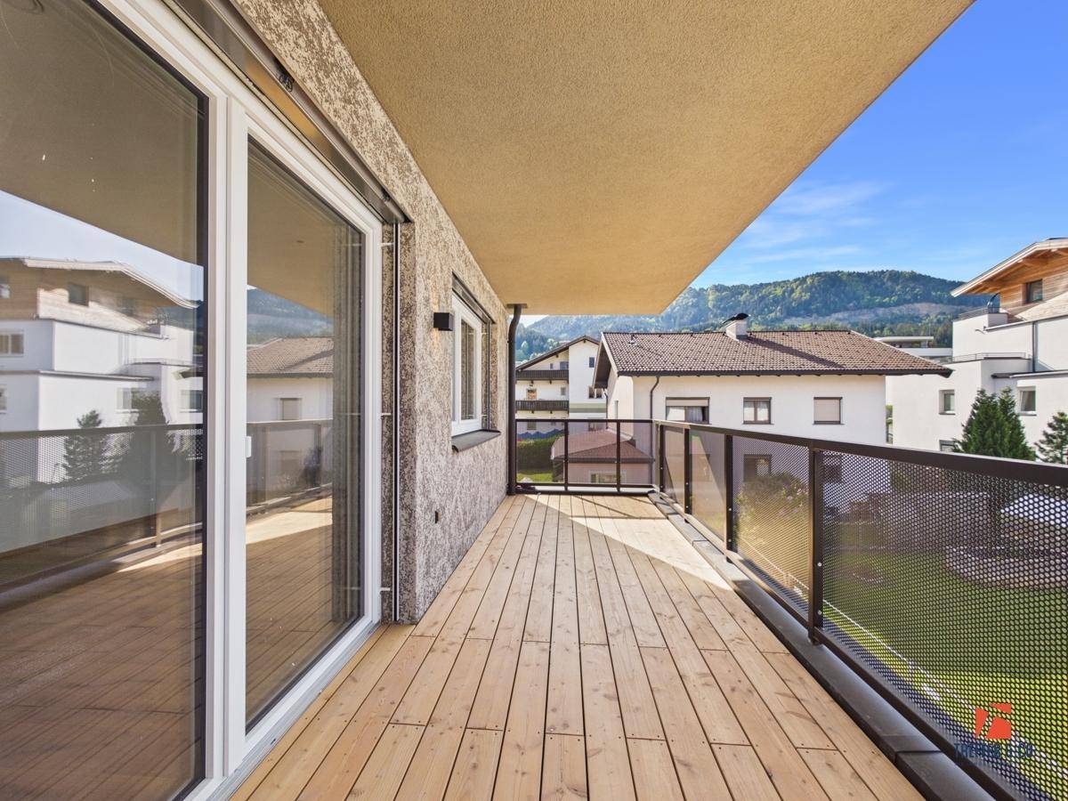 Geräumiger Balkon mit Holzboden, Glasgeländer und Bergblick.