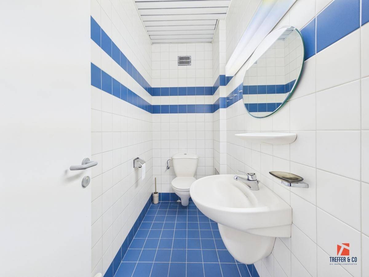 Helles Gäste-WC mit blau-weißen Fliesen, Waschbecken, Toilette und rundem Spiegel.