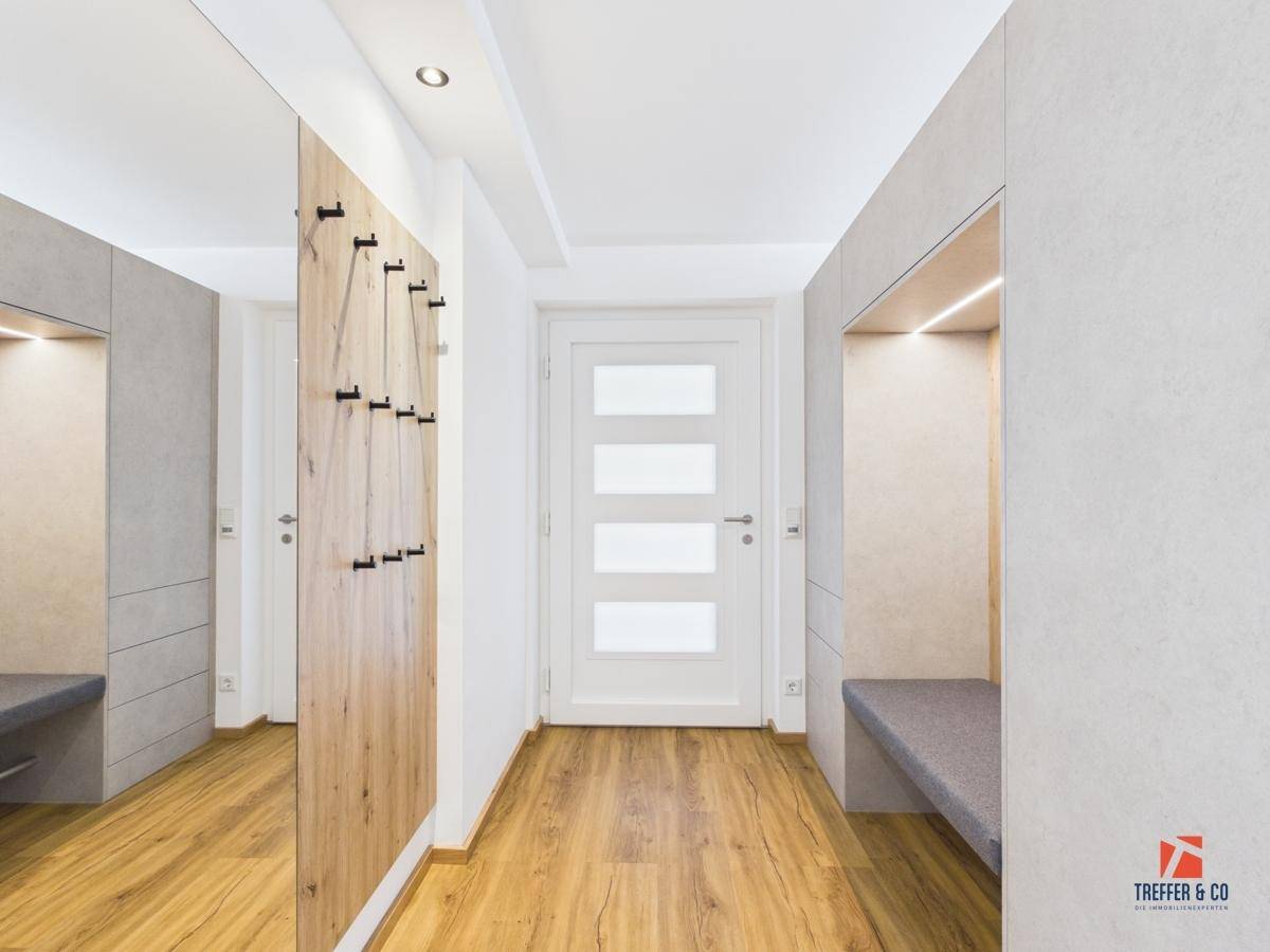 Moderner Eingangsbereich mit integrierter Garderobe, Sitzbank und großem Spiegel.