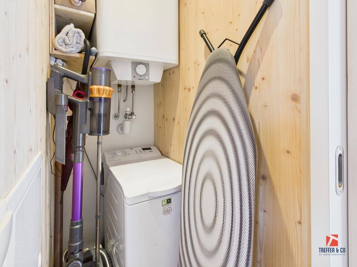 Praktischer Hauswirtschaftsraum mit Waschmaschine, Warmwasserboiler und Stauraum.