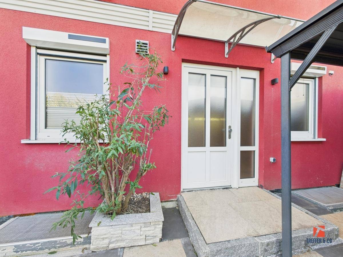 Eingangsbereich des Hauses mit roter Fassade, weißer Tür und einem kleinen Vordach.
