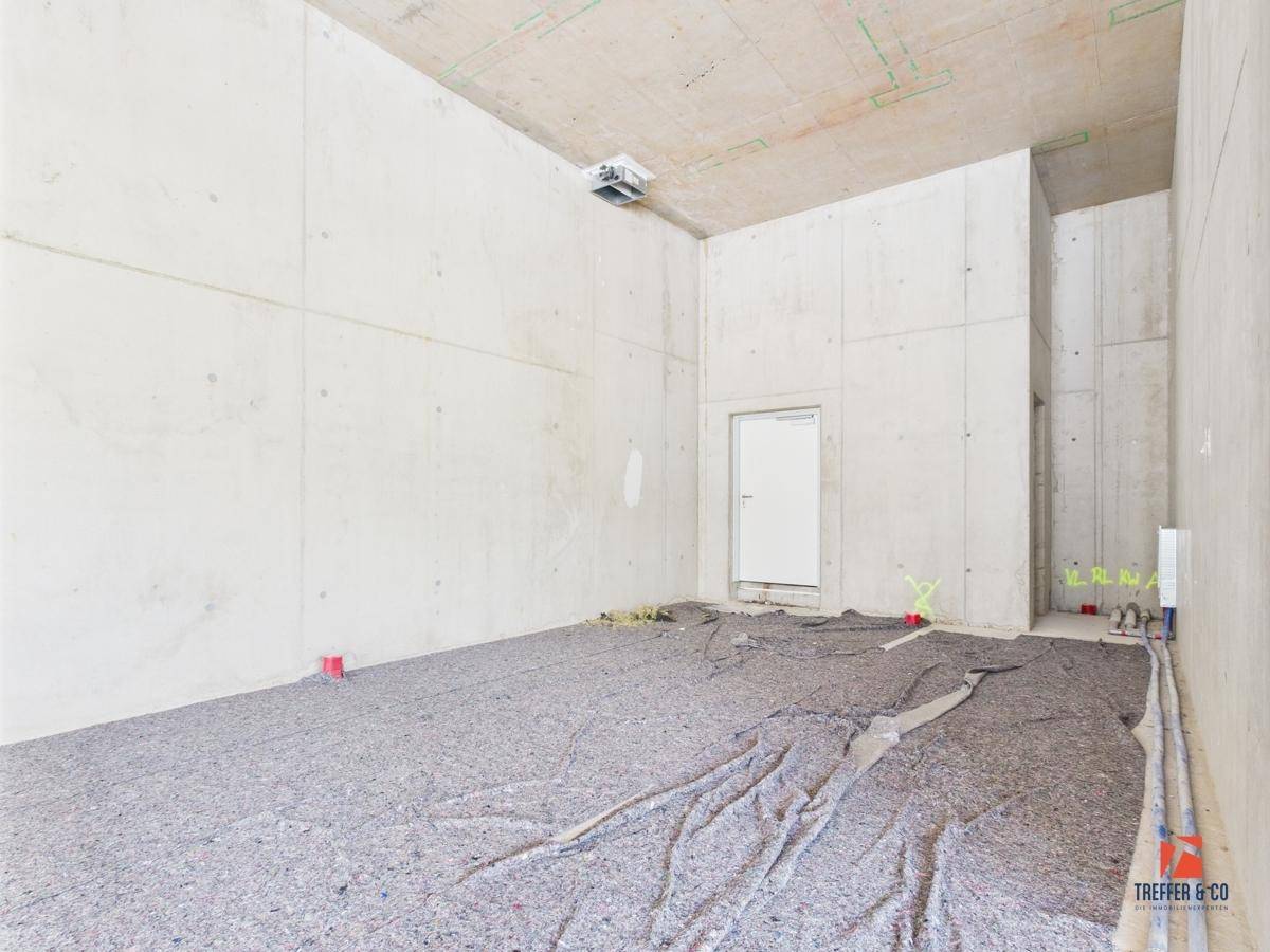 Großer Gewerberaum im Rohbau mit Betonwänden und -decke, vorbereitet für den weiteren Ausbau.