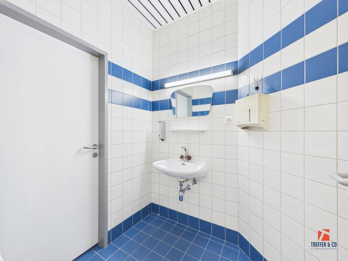 Sanitäre Einrichtung mit weißen und blauen Fliesen, einem Waschbecken und einem Spiegel.