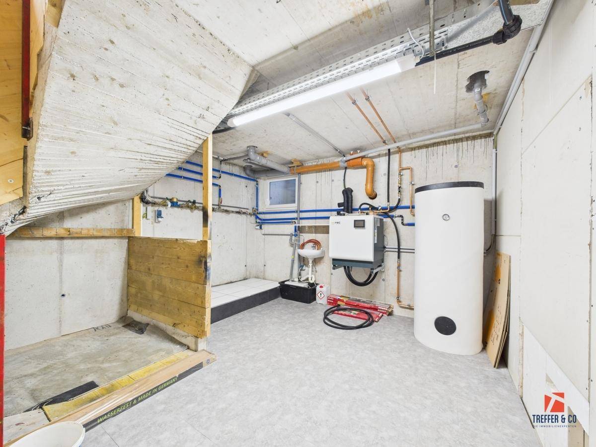 Technikraum im Keller mit Heizungsanlage, Warmwasserspeicher und sichtbaren Leitungen.