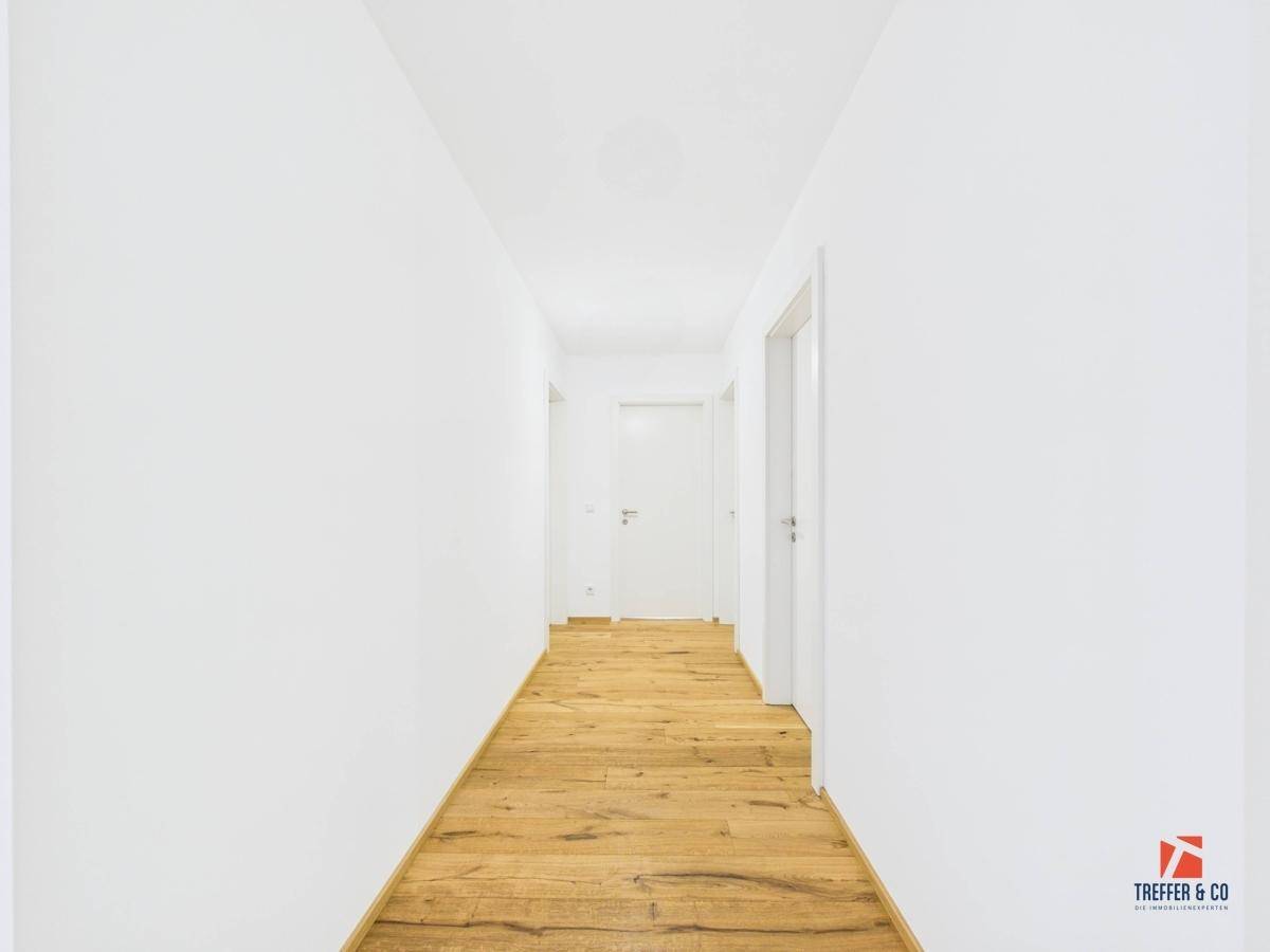 Langer, heller Flur mit Holzboden und weißen Wänden.