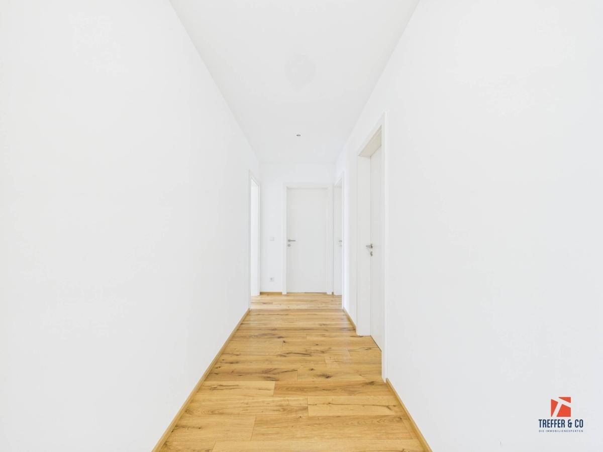 Langer, heller Flur mit Holzboden und weißen Wänden, der zu verschiedenen Räumen führt.
