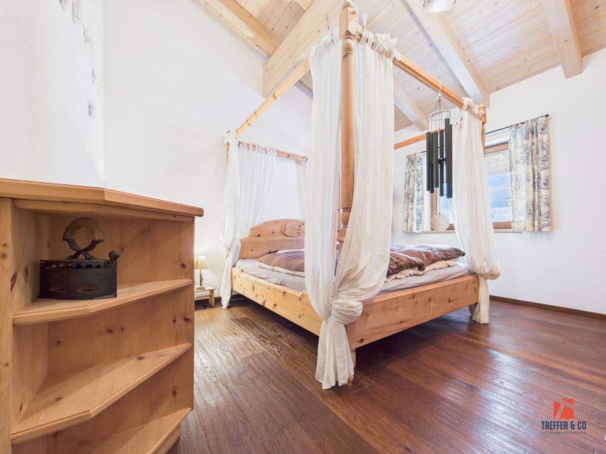 Schlafzimmer mit Holzbalkendecke, Himmelbett und Holzboden, das eine warme Atmosphäre bietet.