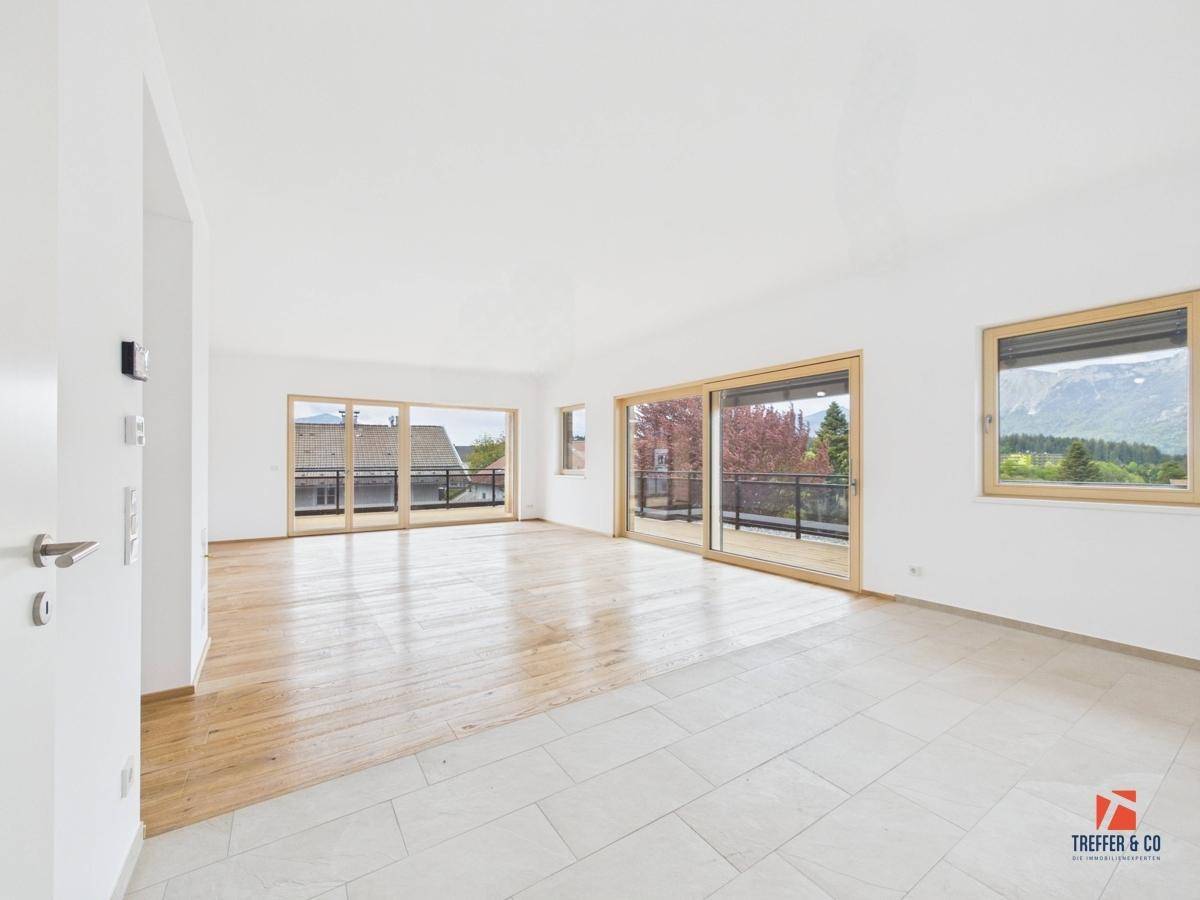 Heller, leerer Wohnraum mit Holzboden, großen Schiebetüren und Zugang zum Balkon.