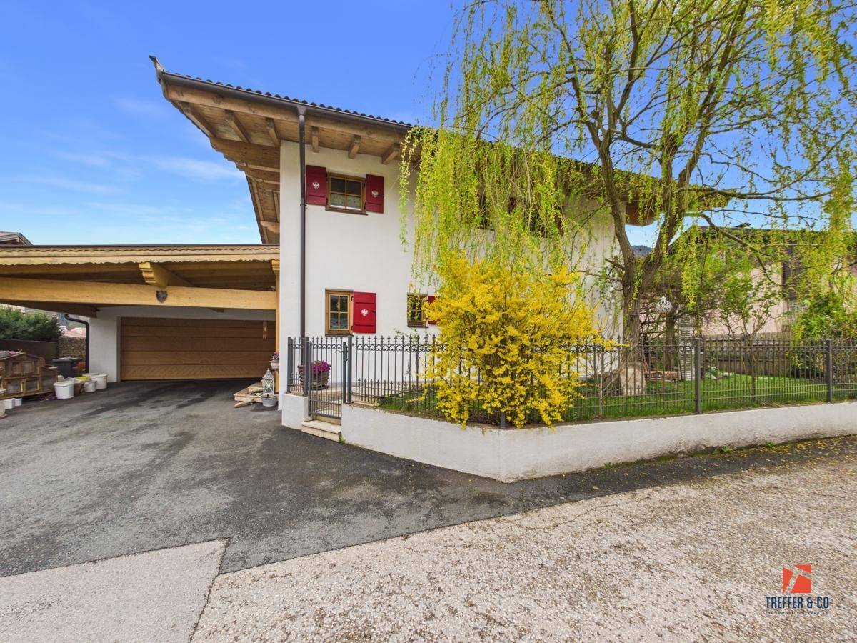 Hausansicht mit gepflasterter Auffahrt, grünem Vorgarten und traditionellen roten Fensterläden.