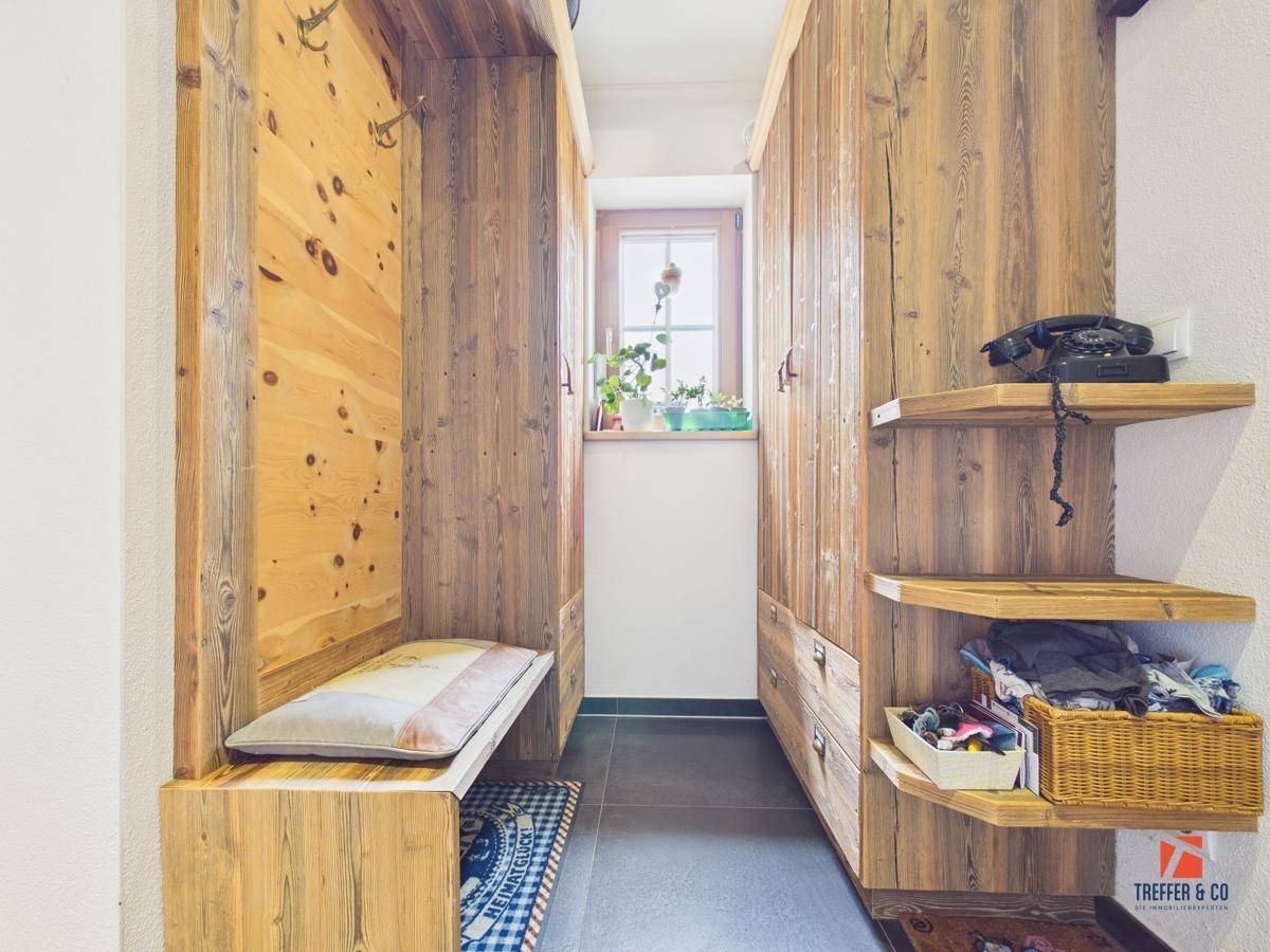 Rustikaler Flur mit Holzeinbauten, Sitzbank und einem kleinen Fenster, das Tageslicht hereinlässt.