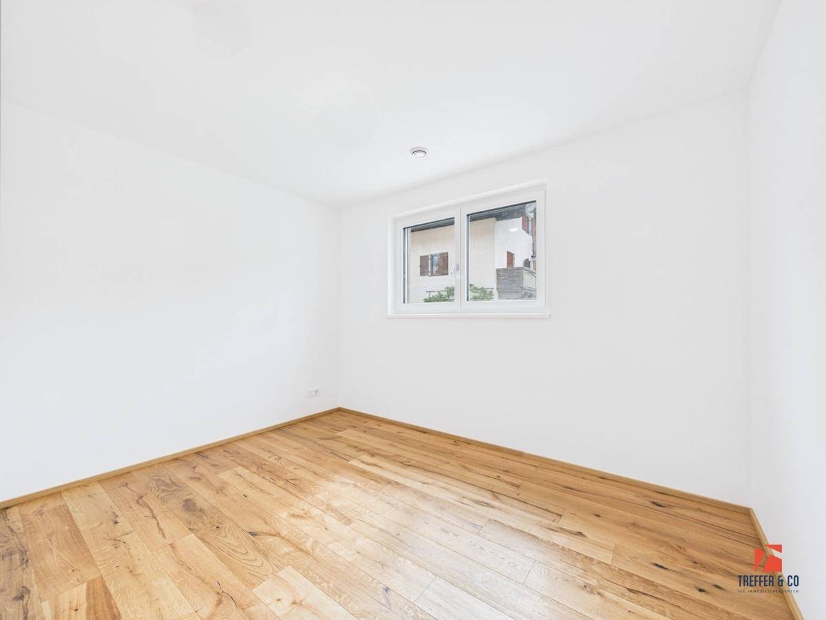 Helles Schlafzimmer mit Holzboden und einem Fenster, das viel Tageslicht hereinlässt.