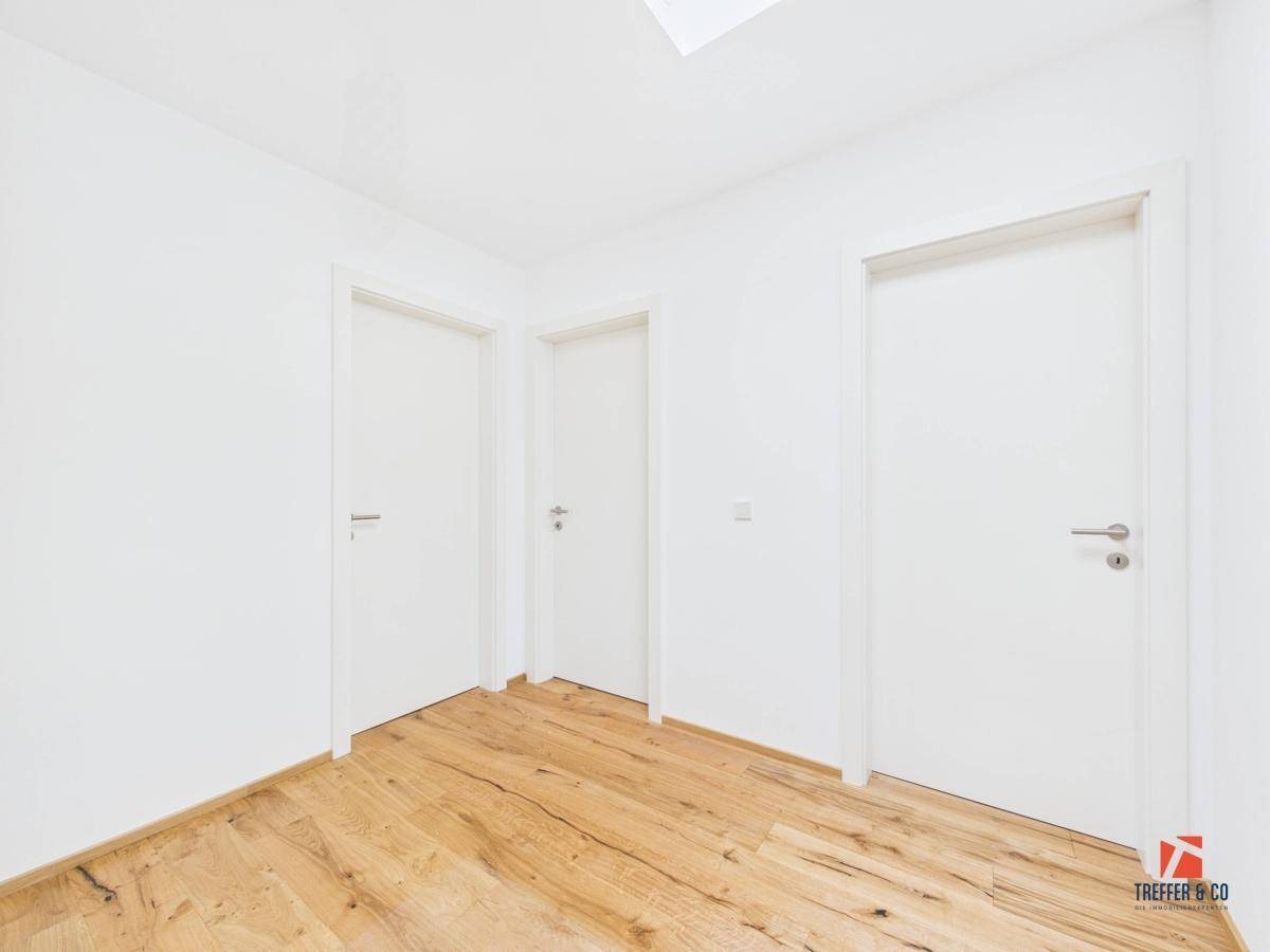 Heller Flur mit Holzboden und drei weißen Türen, die zu verschiedenen Räumen führen.