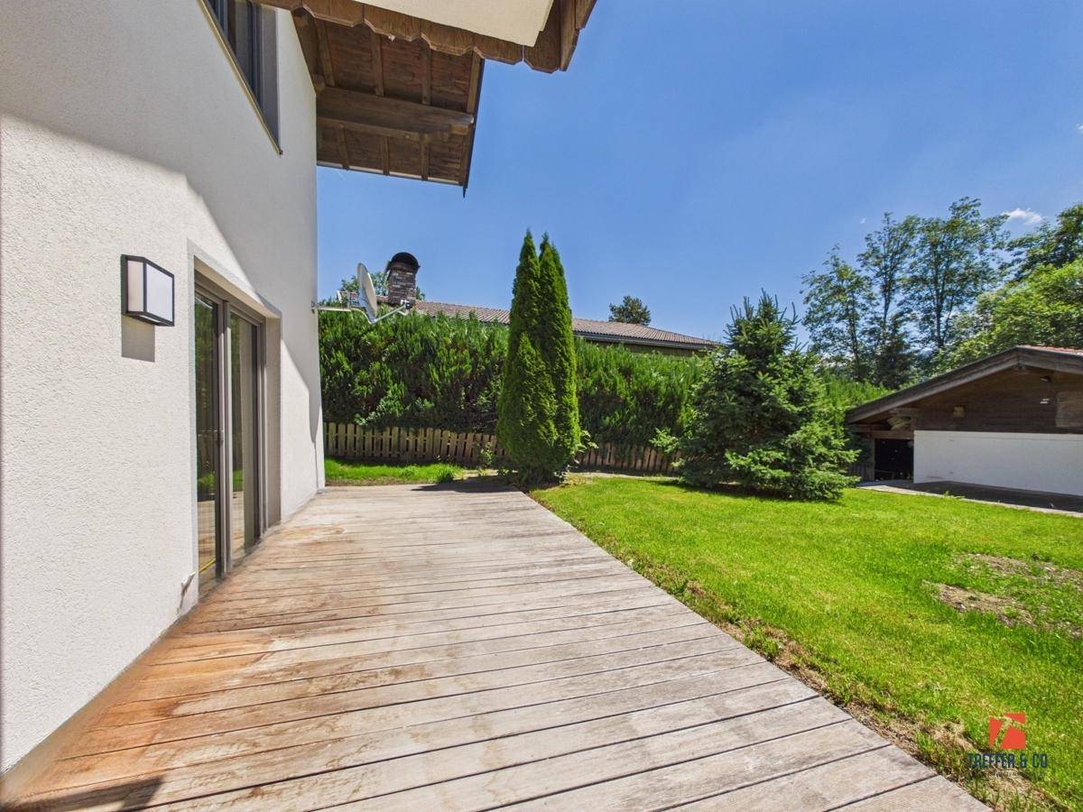Große Holzterrasse mit Zugang zum Garten, umgeben von grüner Hecke.