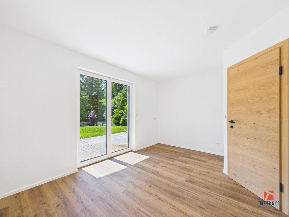 Helles Zimmer mit Holzboden und Zugang zu einer Terrasse oder dem Garten.
