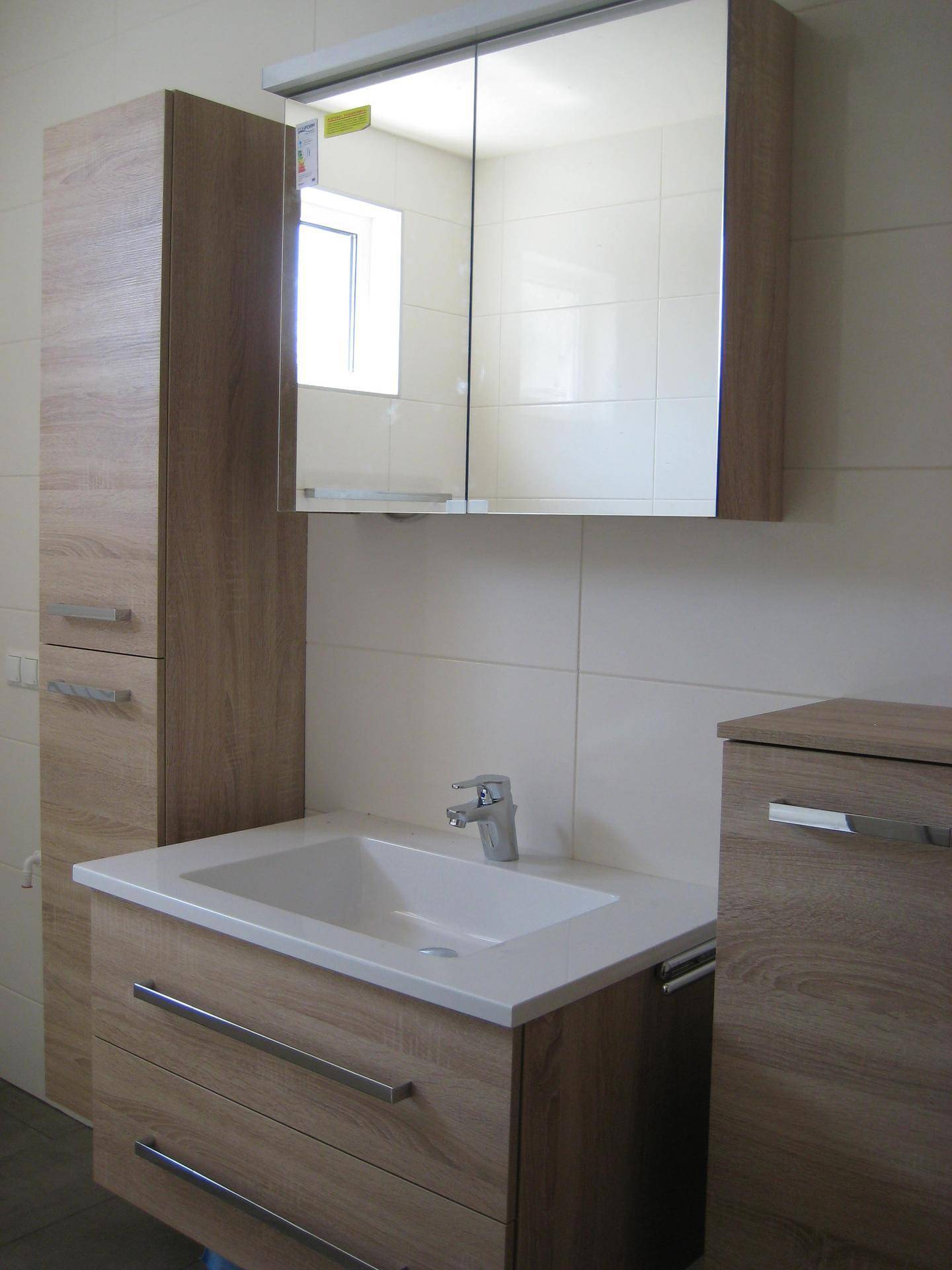Helles Badezimmer mit modernem Waschtisch, Spiegelschrank und Holzoptik-Möbeln.