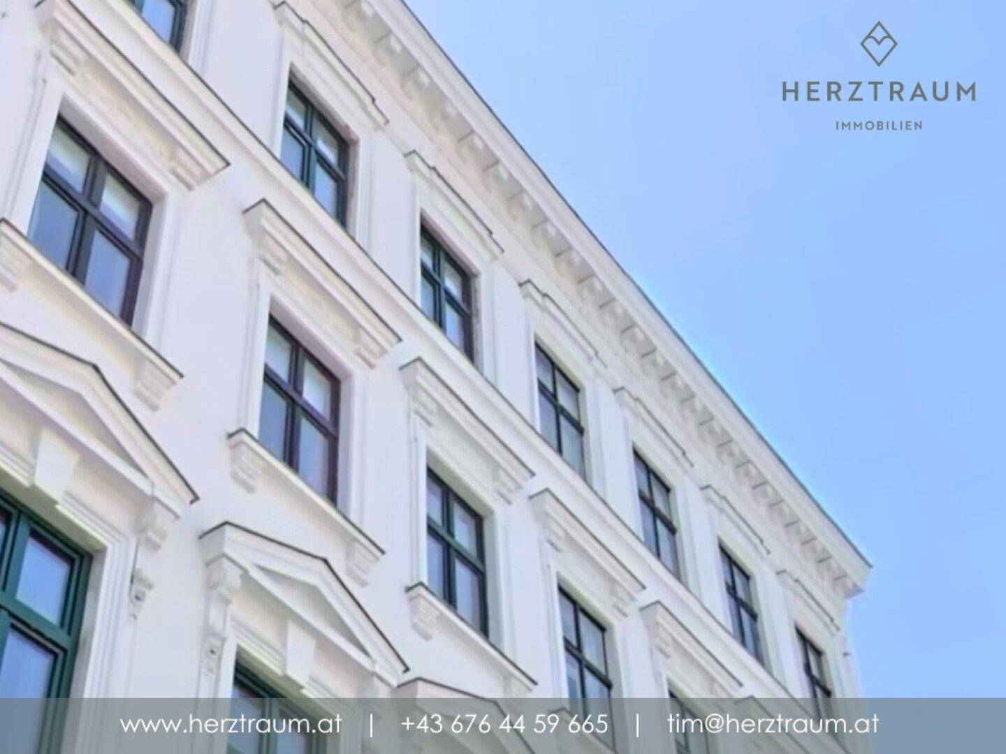 Detailansicht der weißen Altbaufassade mit eleganten Fensterumrandungen unter blauem Himmel.