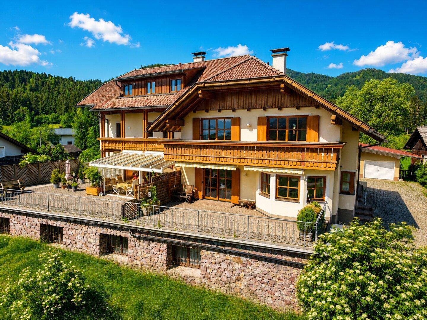 Großzügige Terrasse mit Balkon und Bergblick, umgeben von grüner Landschaft und einem gepflegten Garten.