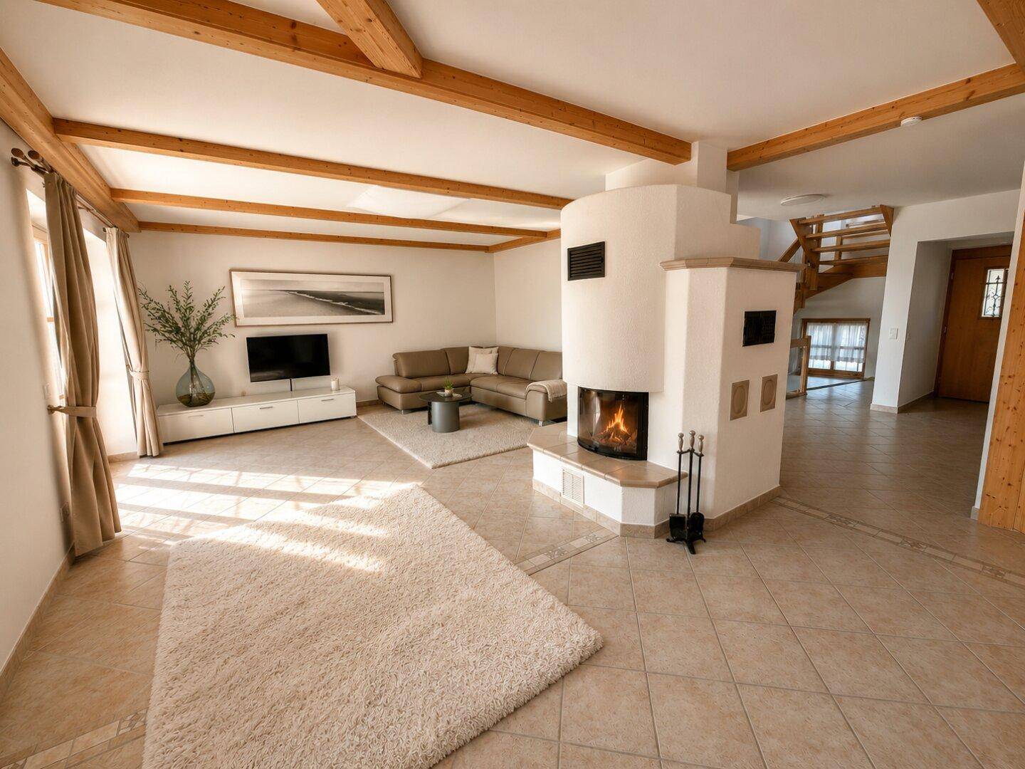 Gemütliches Wohnzimmer mit Kamin, bequemer Couch und rustikalen Holzbalken an der Decke, lichtdurchflutet.