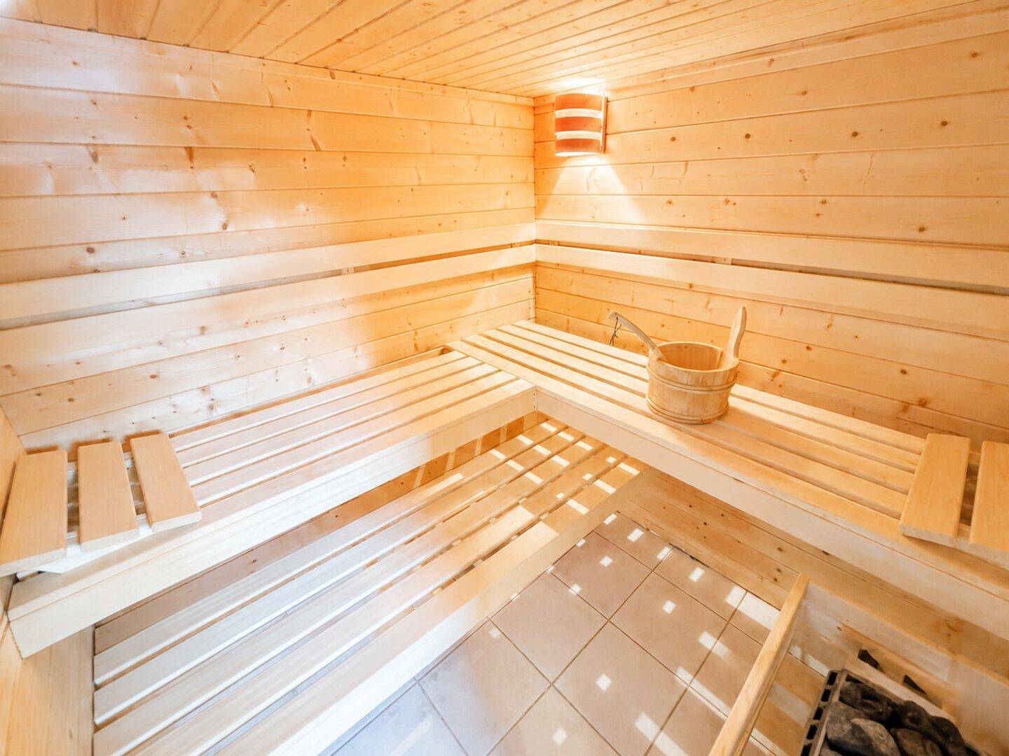 Innenansicht der holzvertäfelten Sauna mit Sitzbänken und Saunaofen, ein Ort der Ruhe.