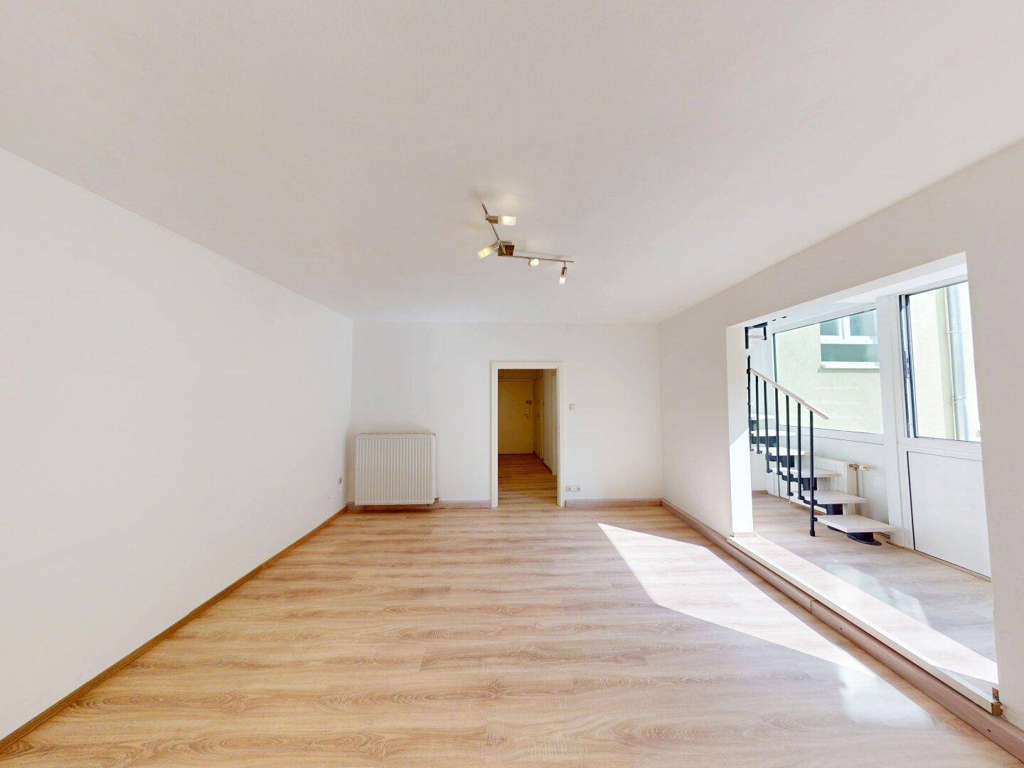 Wohnzimmer mit Laminatboden, Heizkörper und Treppenzugang zu einem erhöhten Bereich.