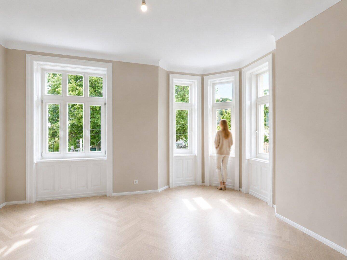 Geräumiges Wohnzimmer mit Fischgrätparkett und hohen Fenstern, die viel Tageslicht hereinlassen.