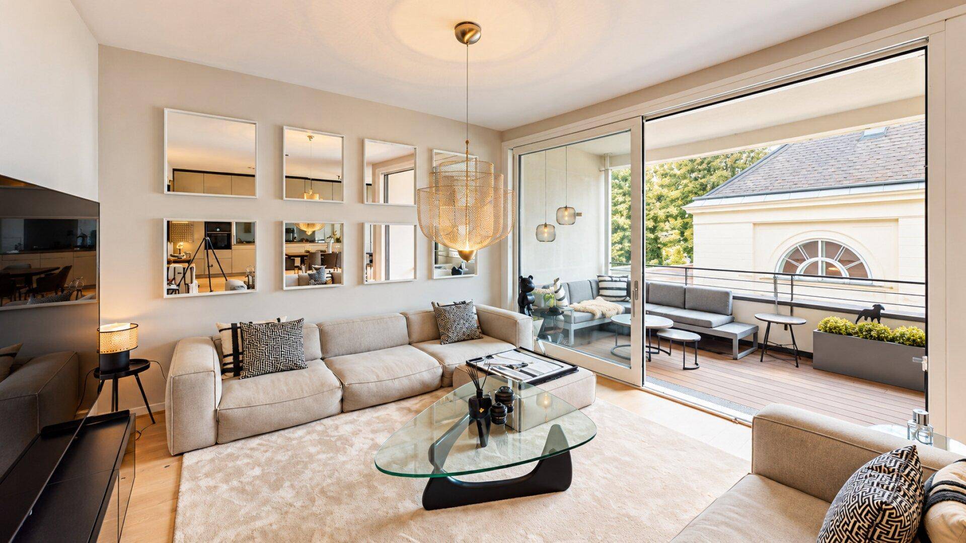 Gemütliches Wohnzimmer mit großem Sofa, Teppichboden und Schiebetür zum möblierten Balkon.